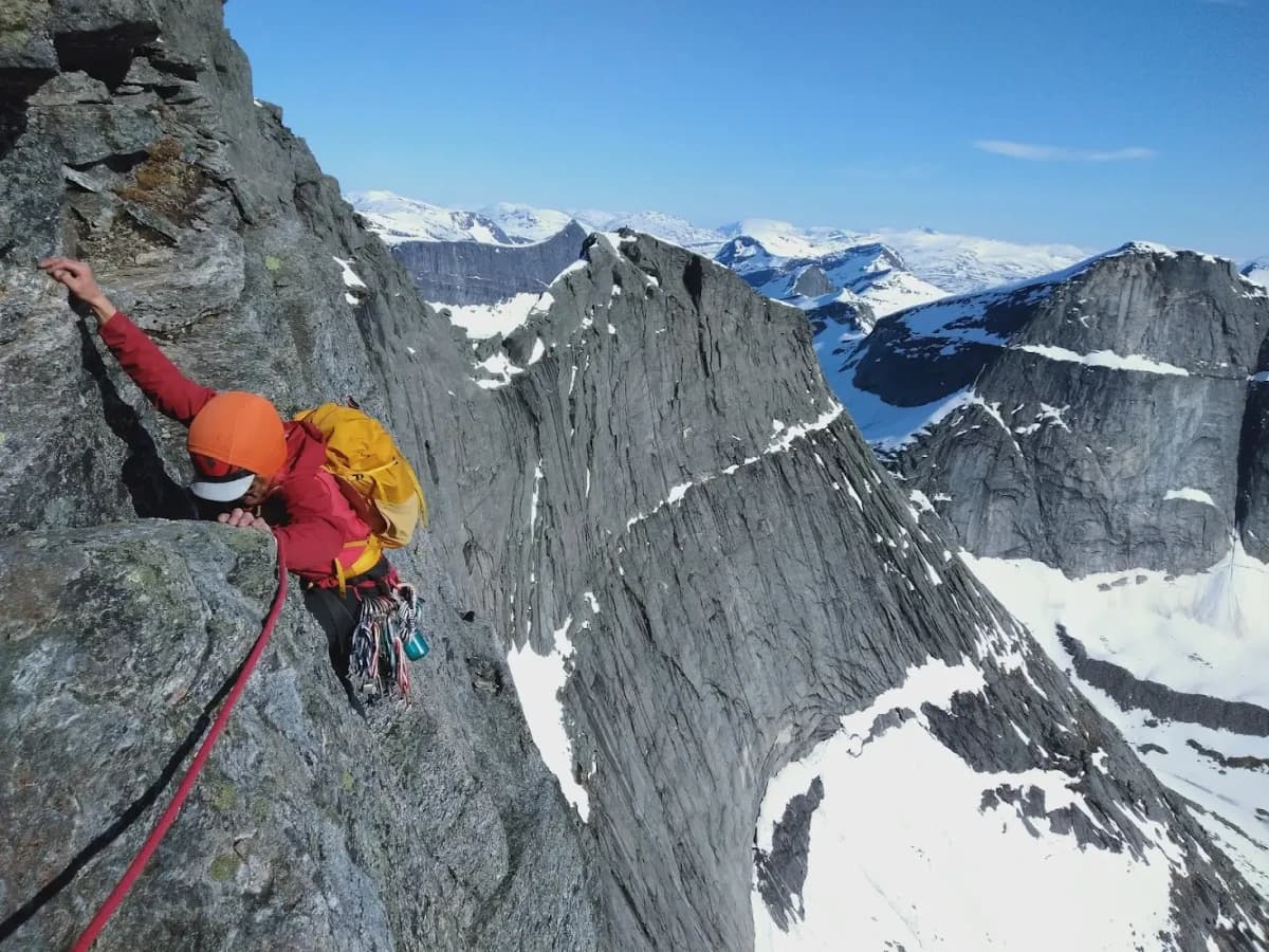 A red-jacketed climber on granite at Stetind, with steep mountains behind