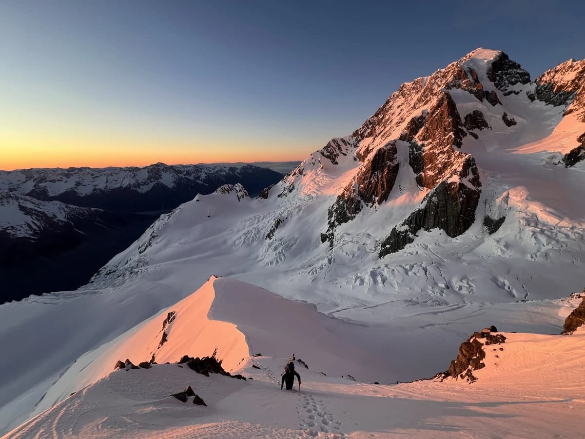 A small climber beneath a vast mountain face illuminated by sunrise